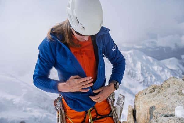 Climber checking her gear on a snowy mountain peak in outdoor adventure settings.