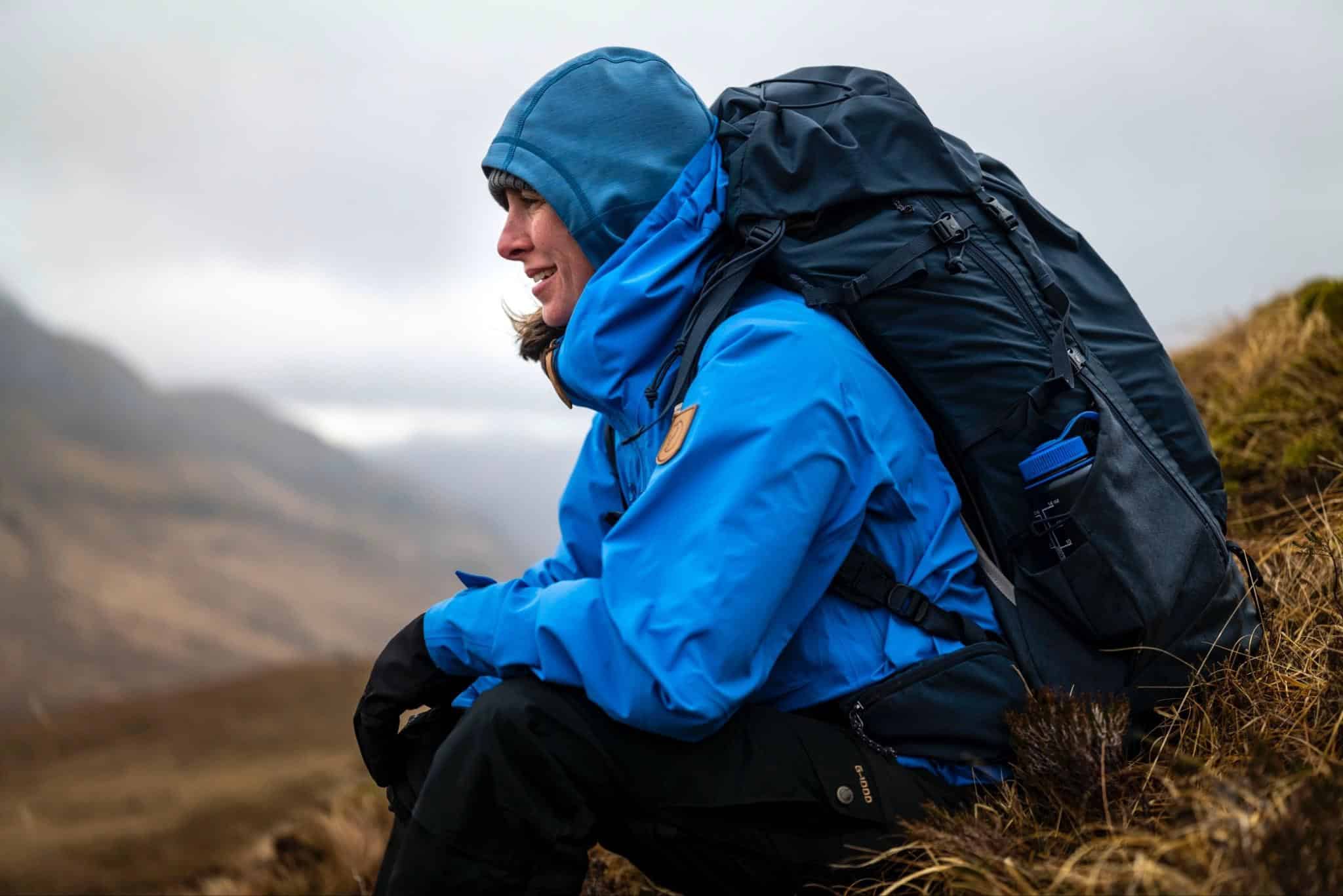 Bright blue waterproof outdoor jacket with hood, worn by hiker in wilderness.