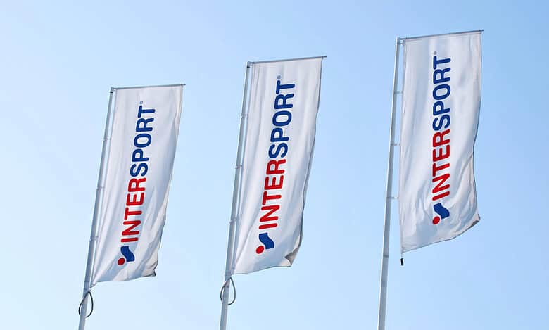 Three Intersport flags flying in the wind at an outdoor sports event.