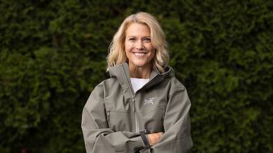 1. Woman in outdoor waterproof jacket smiling, lush green background.