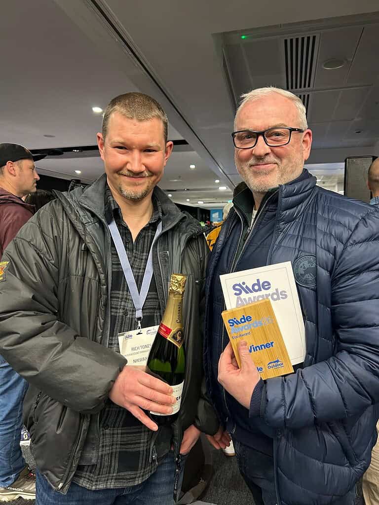 Two men at the Green Apple Awards holding a bottle of champagne and a trophy.