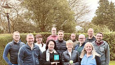Group of people outdoors holding awards and a tennis ball.