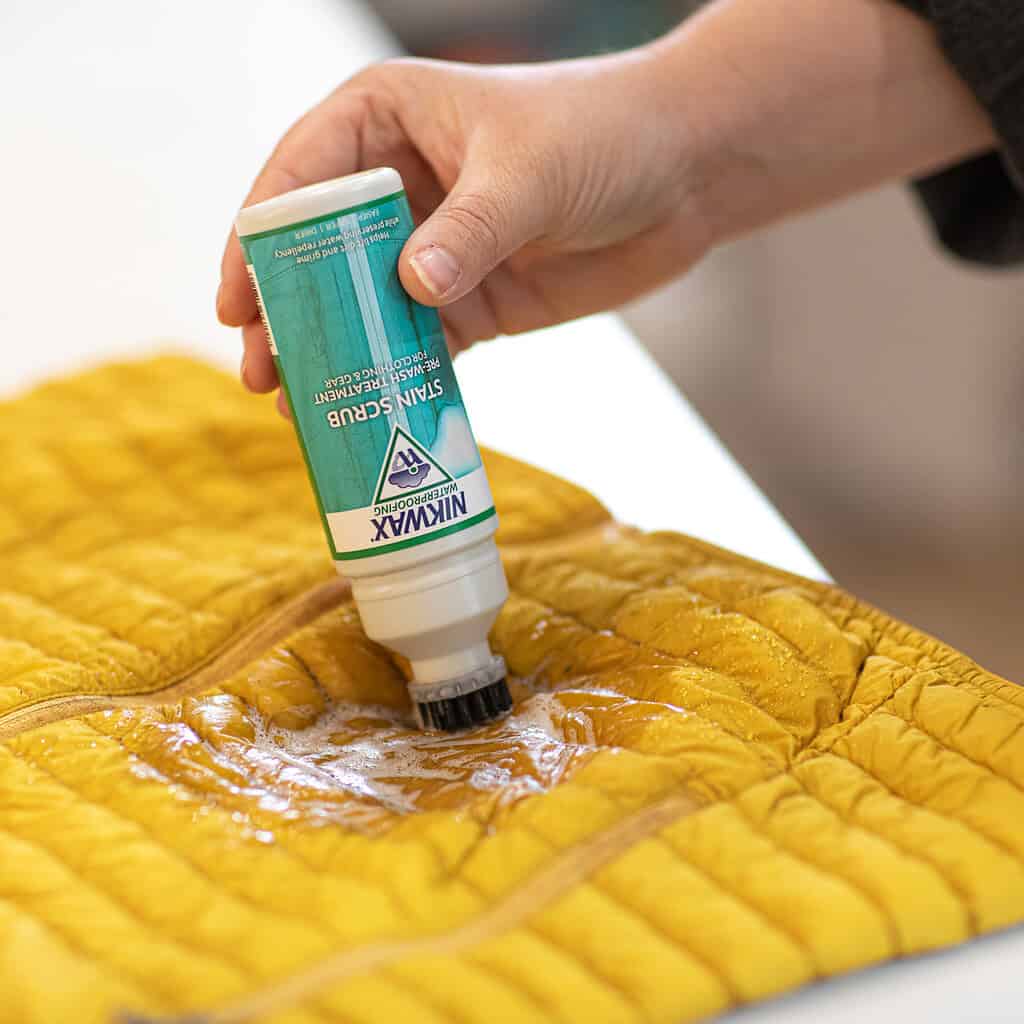 Applying Nikwax waterproofing treatment to a yellow quilted outdoor jacket.