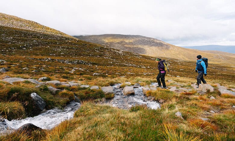 Two hikers walking through a rugged landscape in the Scottish Highlands.