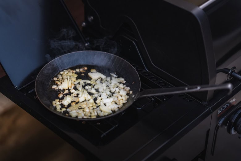 Outdoor gas barbecue grill with sizzling onions.