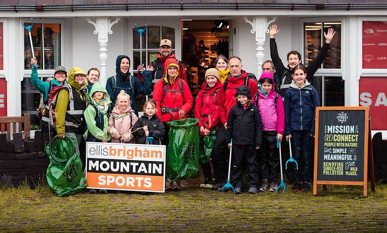 Group of hikers with backpacks outside a shop, smiling and waving.