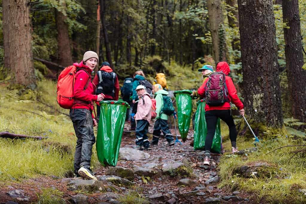 Group of children and adults hiking in a forest with outdoor gear and backpacks.