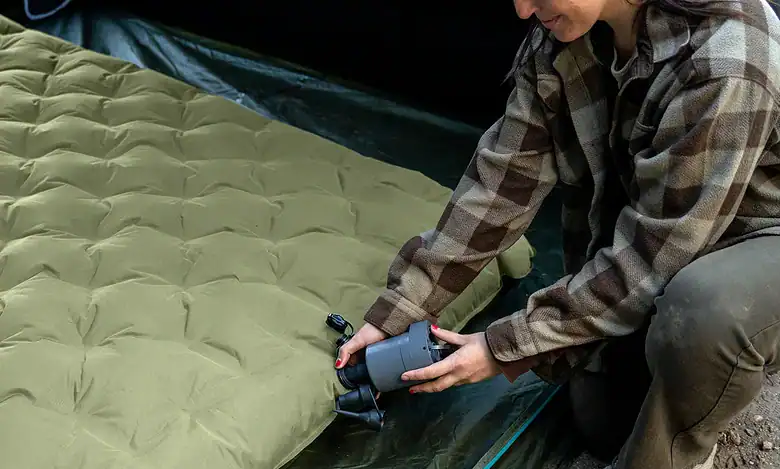 Woman inflating a camping mattress outdoors with a pump.