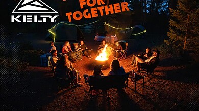 Enjoying a campfire with friends in a forest setting at night, surrounded by tents and outdoor gear.
