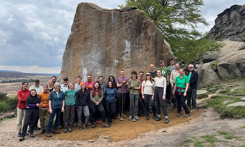 Group of hikers and outdoor enthusiasts in front of a large rock formation.