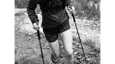 Female hiker trekking on mountain trail with trekking poles in outdoor landscape.