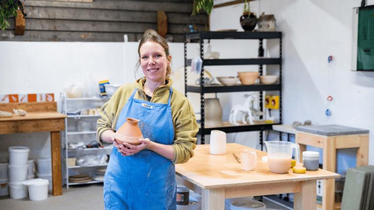Woman holding a clay pot in a pottery studio at Quex Park.