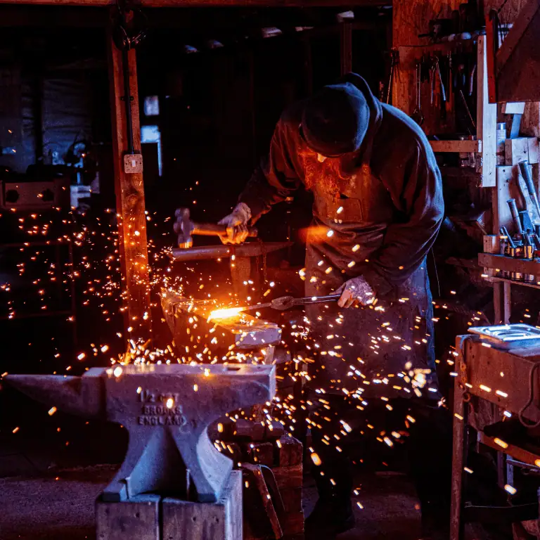 Blacksmith forging metal with sparks flying in a workshop.