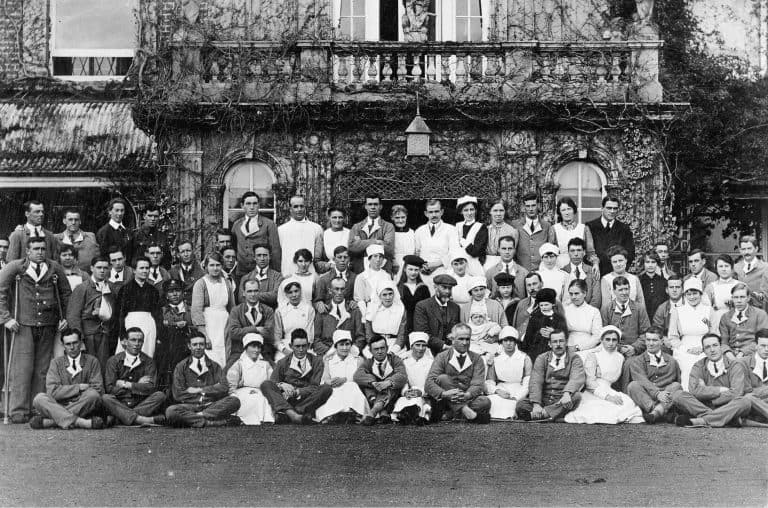 Historical black and white group photo outside a large estate building.