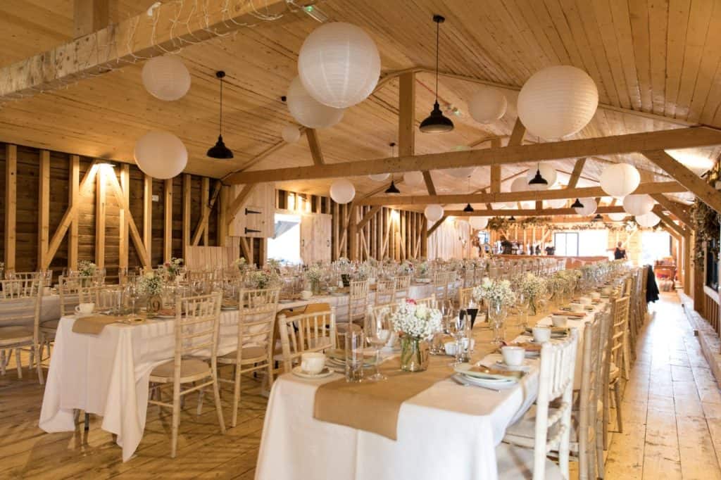 Elegant wedding reception setup in a rustic barn with hanging paper lanterns.