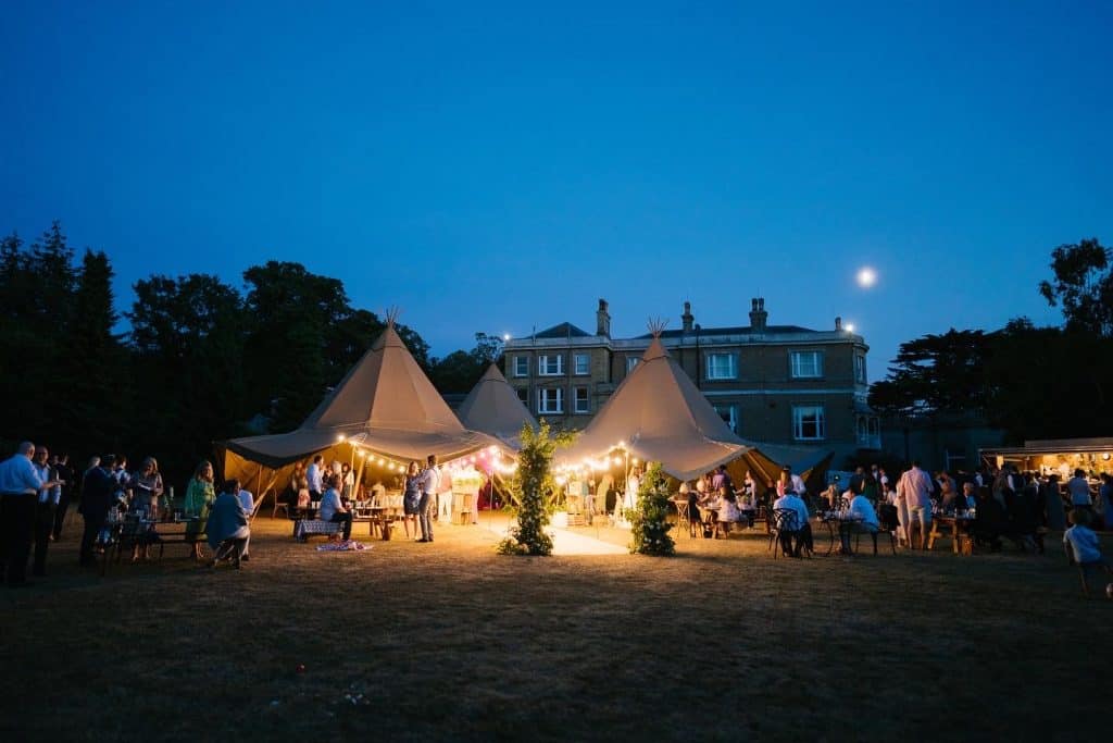 Tents and guests at an outdoor wedding reception during the evening at Quex Park.