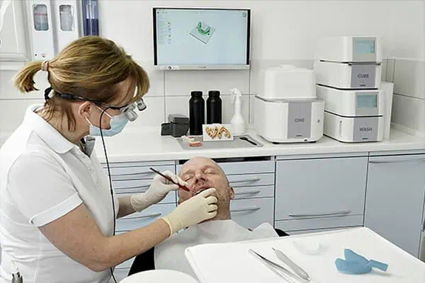The ONE 3D Printing Solution, including the ONE wash and the ONE cure, RS Print Studio, and dental resins in a clinic, while the doctor works on a patient