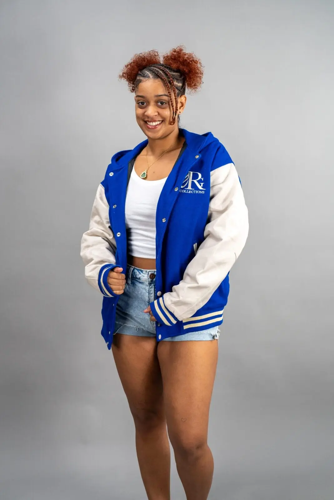 Comfortable young woman wearing Reign Gear LLC varsity jacket, smiling confidently.