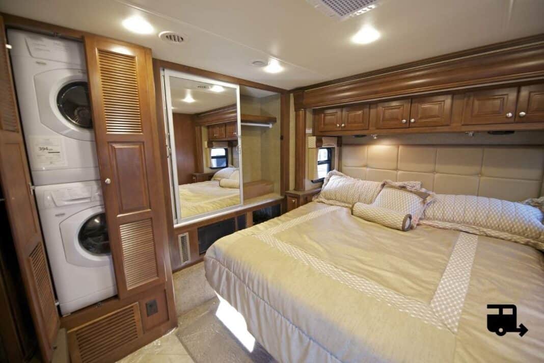 High-quality RV bedroom featuring a comfortable bed, built-in wooden cabinetry, and integrated washer/dryer for convenient living on the road. Perfect for travelers seeking comfort and practicality in their motorhome or travel trailer.