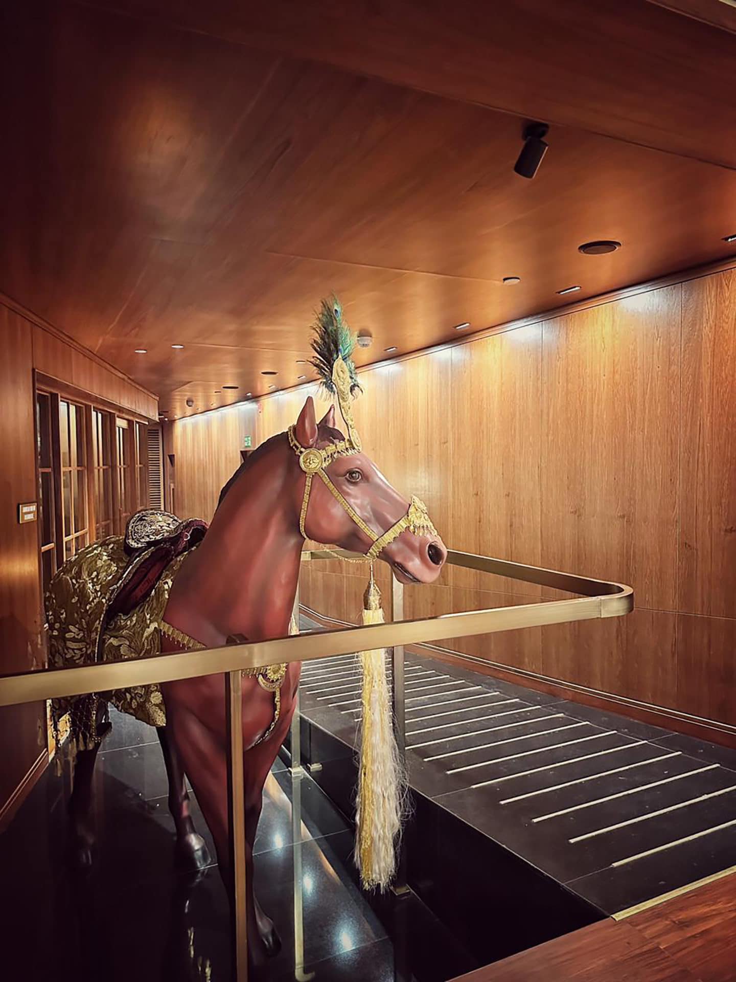 Decorative horse sculpture with ornate saddle and feathered headpiece in wooden interior.