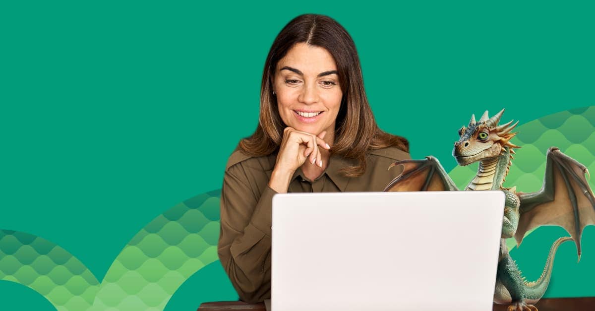 A woman with a smile is sitting at a desk, looking at her laptop. There is a green dragon standing next to her.