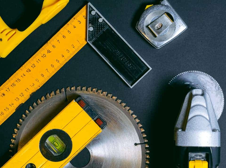 A collection of various tools arranged on a black surface, including measuring sticks and auto parts, featuring yellow elements.