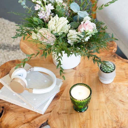 A big vase of flowers on a wooden coffee table, next to some headphones, a candle and a journal. All ready for a self care 30 day challenge