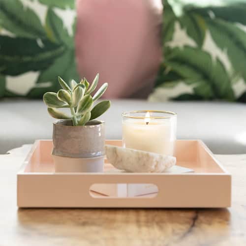 A wooden tray on a coffee table containing a candle, a potted plant and our self care day checklist
