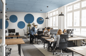 Modernes Großraumbüro mit mehreren Personen bei der Arbeit an Schreibtischen; an der Wand große, runde Akustikelemente zur Verbesserung der Raumakustik.