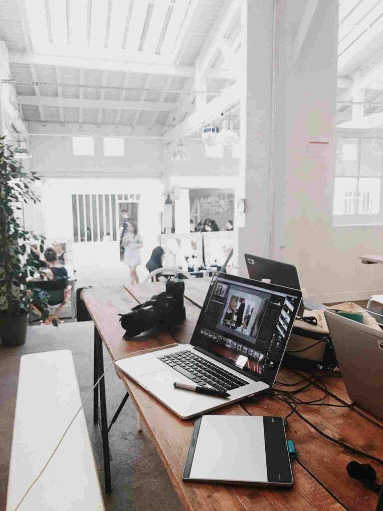 Laptop-Arbeitsplatz in modernem Großraumbüro mit viel Tageslicht und industrieller Architektur – Beispiel für akustisch herausfordernde Büroumgebung.
