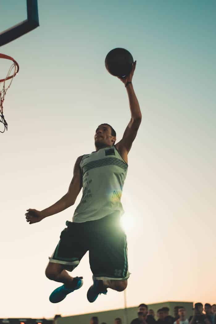 about-us Basketball player performing a powerful dunk during sunset on an outdoor court.