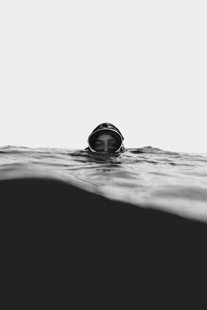 heros-img A monochrome photograph of a diver's face emerging from the water, creating a dramatic and moody scene.