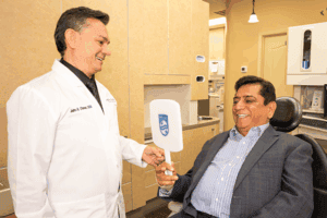 A patient looks at his smile on a small mirror while Dr. Chavez looks on.