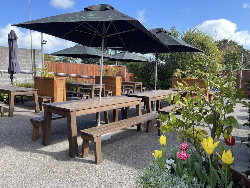 Outdoor patio with wooden tables, benches, and large umbrellas at Stumble Inn NZ.