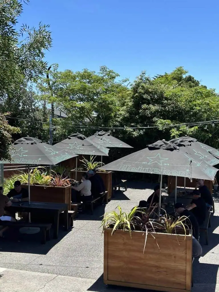 Outdoor seating area at Stumble Inn with Heineken umbrellas and lush greenery NZ.