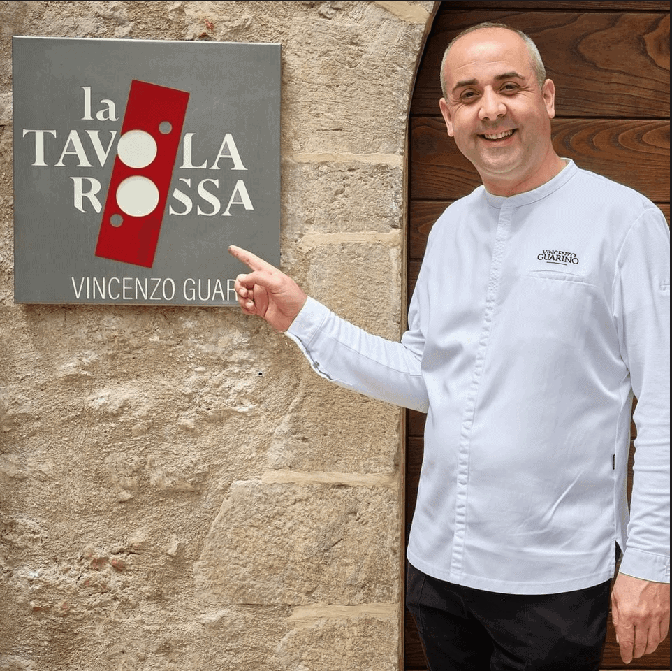 Journey Through the Green Heart of Italy: An Itinerary to Discover Umbria image qui montre le chef vincenzo guarino indiquer la plaque de son restaurant la tavola rossa au sein de la maison teritoria castello di postignano