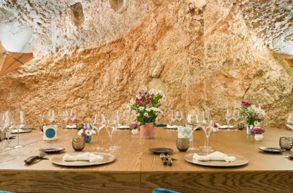 Journey Through the Green Heart of Italy: An Itinerary to Discover Umbria vue d'une des tables du restaurant la tavola rossa au sein de castello di postignano. large table en bois entourée de murs en pierre et habillée de façon élégante.