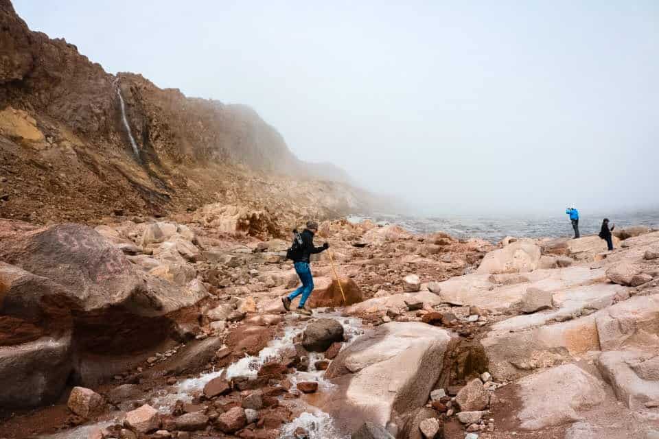 A hiker traipsing across the rocky landscape beside Santa Isabel Glacier with fog in the distance.
