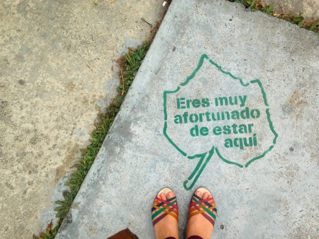 Colorful sandals stand in front of a painted sidewalk stating "Eres muy afortunado de estar aqui" which in English means "You are very fortunate to be here"