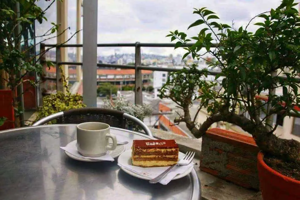 A coffee and tiramisu sit on a table overlooking the city of Manizales from the balcony of a restaurant.