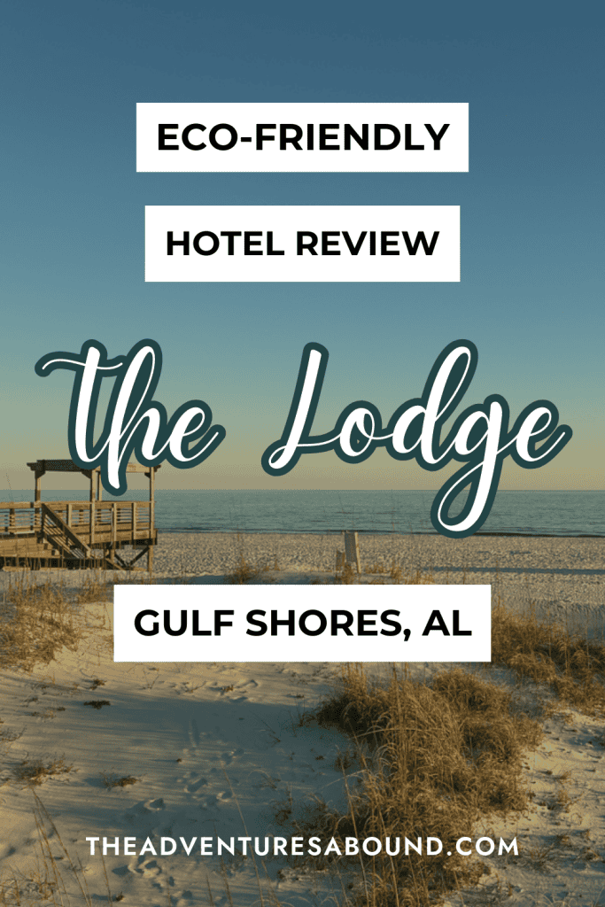 The image is a Pinterest-style pin promoting an eco-friendly hotel review of "The Lodge" in Gulf Shores, Alabama. It features a beach scene with sand dunes, sea grass, and a wooden boardwalk leading toward the ocean under a clear blue sky. Overlaid text reads: "Eco-Friendly Hotel Review," "The Lodge," and "Gulf Shores, AL." At the bottom, the website URL "theadventuresabound.com" is displayed.