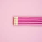 Four pink pencils with erasers are aligned horizontally on a light pink background, perfect for jotting down different types of journaling prompts for mental health.