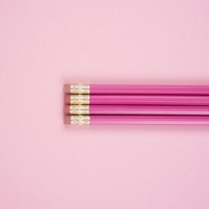 Four pink pencils with erasers are aligned horizontally on a light pink background, perfect for jotting down different types of journaling prompts for mental health.