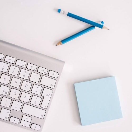 A collection of blue stationery and tools on a desk with a mac computer. This desk is in use by someone using our daily journal prompts for teens