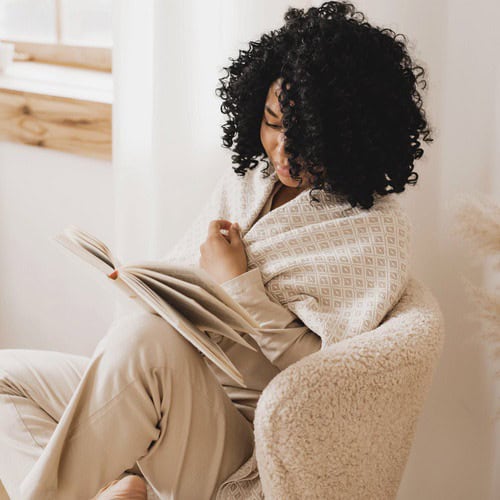 Morning journaling prompts 2 A woman with curly brown hair, dressed in a cream tracksuit, reading a book about morning journaling prompts