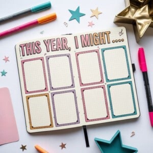An open journal titled this year, i might... Shows eight empty, colorful boxes. Pens, star-shaped decorations, and a gold star dish are scattered on the white table—perfect for journaling at new year.