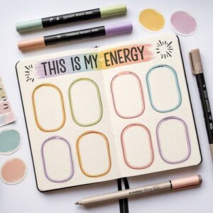 An open bullet journal displays “this is my energy” at the top, with six colorful empty oval sections—perfect for new year manifestation journal prompts. Surrounding the journal are pastel markers, pens, and circular color swatches on a light surface.
