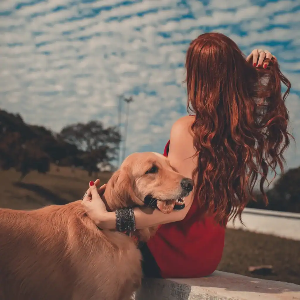 Woman-sitting-down-on-a-wall-with-her-golden-retriever-dog-next-to-her