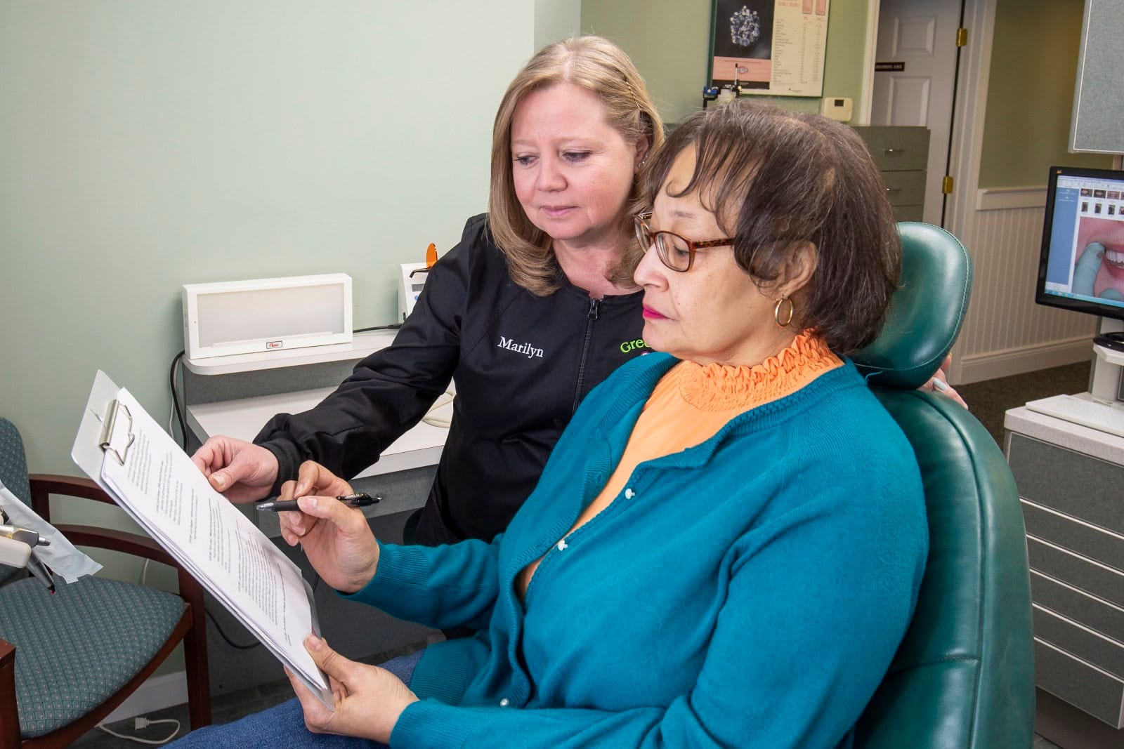A dental assistant shows a patient payment options on a clipboard