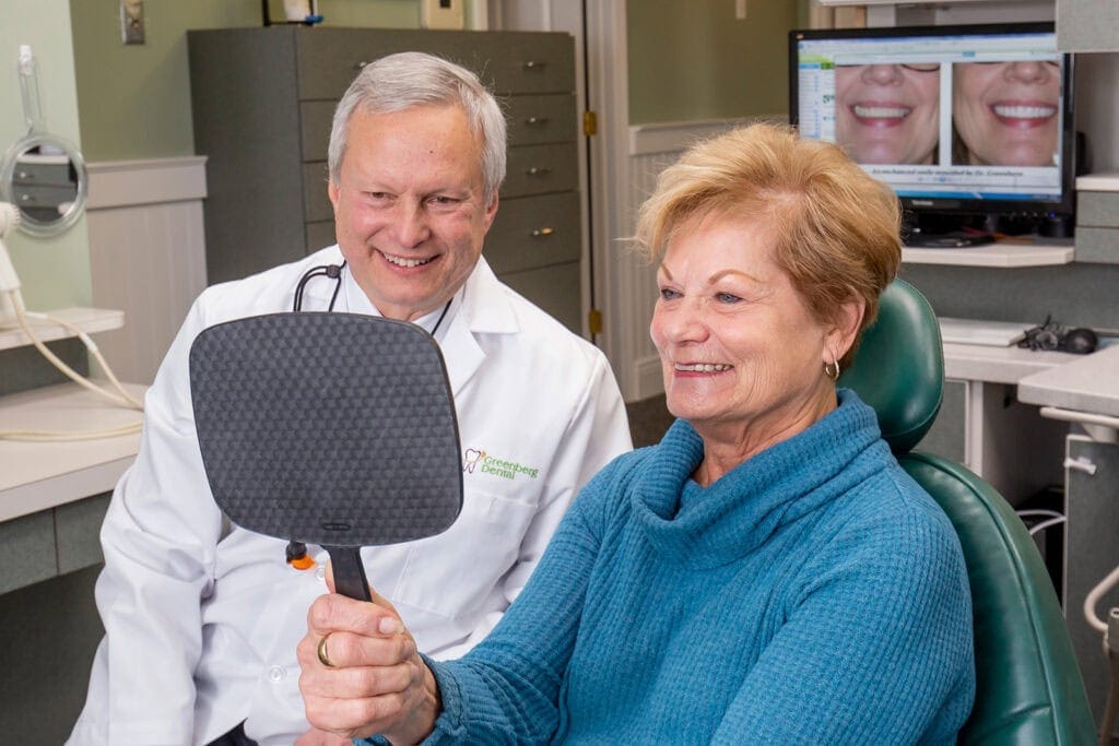 Dr. Randy Greenberg examines a patient checking her smile on a mirror
